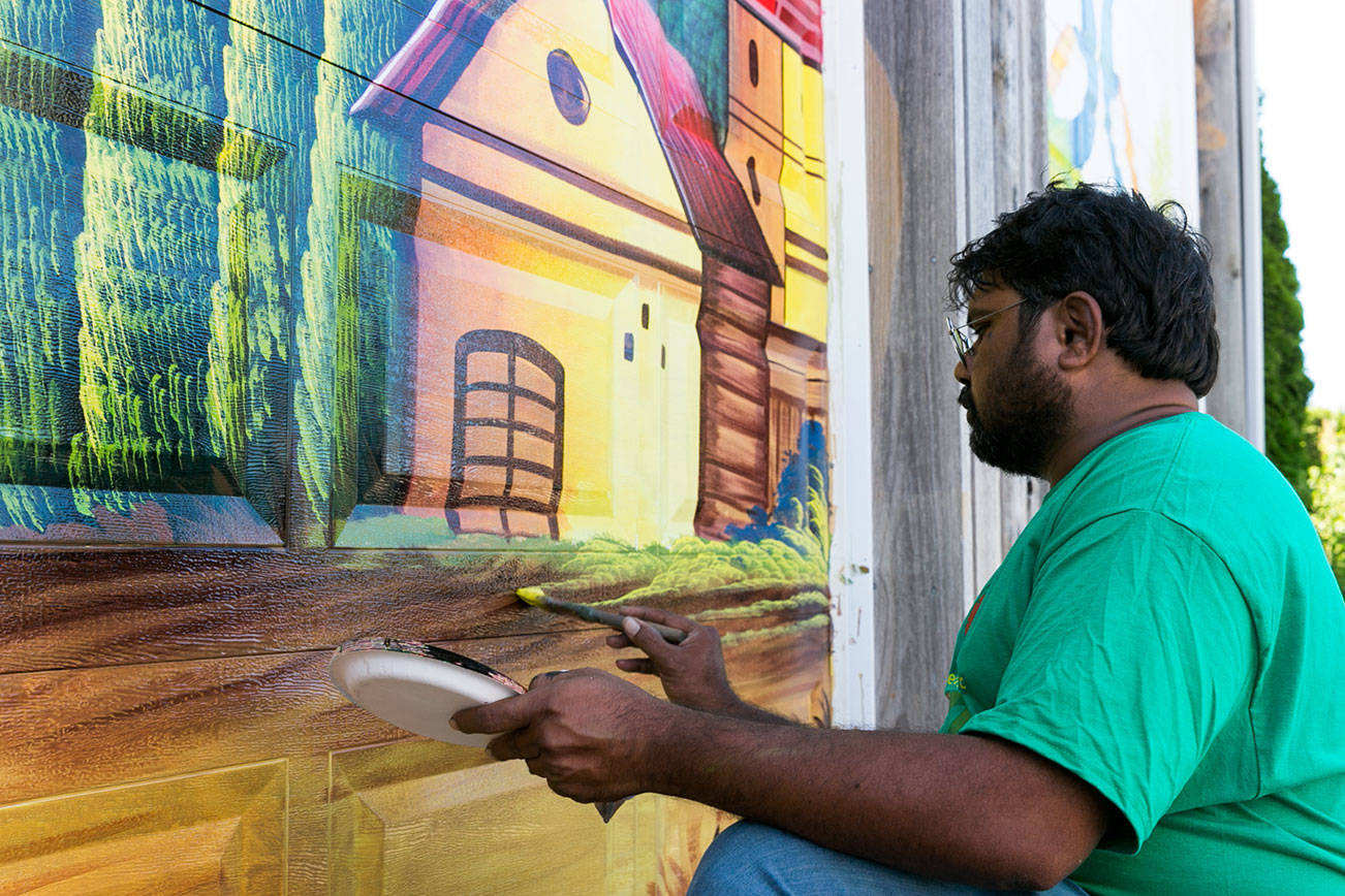 Haider Ali paints the garage doors of Garden Treasures Nursery & Organic Farm in Arlington on Aug. 7. (Kevin Clark / The Herald)