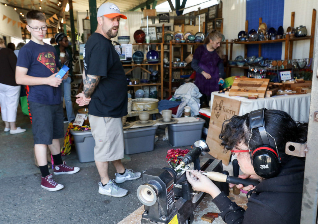 Angela Liberty, who runs Knotty Dog Craftworks with her husband, Stephen, demonstrates how she turns pens by hand on her lathe. (Lizz Giordano / The Herald) 

