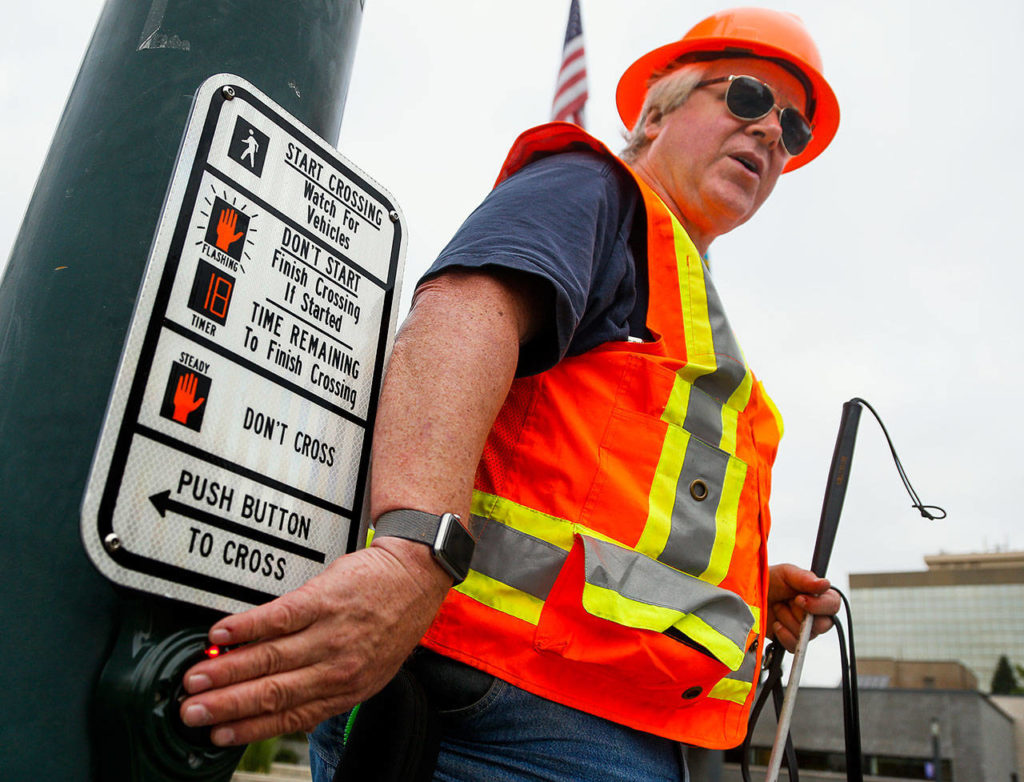 George Basioli presses a button to demonstrate how sound and vibration signals are used to help both hearing- and vision-impaired pedestrians trying to cross a street downtown. (Dan Bates / The Herald)
