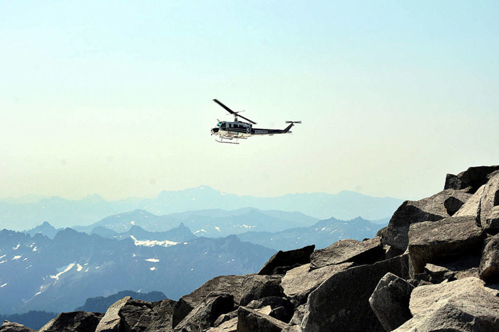 A helicopter crew flies around the summit of Vesper Peak, in the search for missing hiker Sam Sayers, 27, of Seattle. In the background are the Cascade mountains to the southwest of the peak, near Spada Lake. (Caleb Hutton / The Herald)
