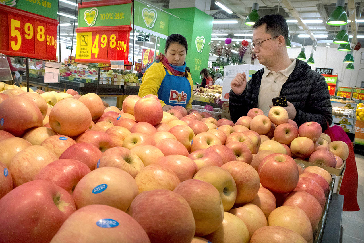 A woman helps a customer shop for apples at a supermarket in Beijing in March. China raised import duties on a $3 billion of U.S. pork, fruit and other products in April in an escalating tariff dispute with President Trump that companies worry might depress global commerce. China imports about $50 million of apples from Washington state growers. (Mark Schiefelbein/Associated Press file photo)