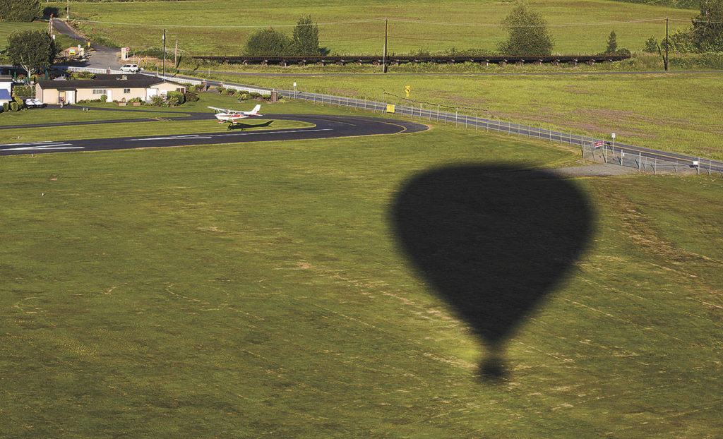 A plane lands on the runway of Harvey Airfield as the shadow of a hot air balloon passes by. (Andy Bronson / The Herald)
