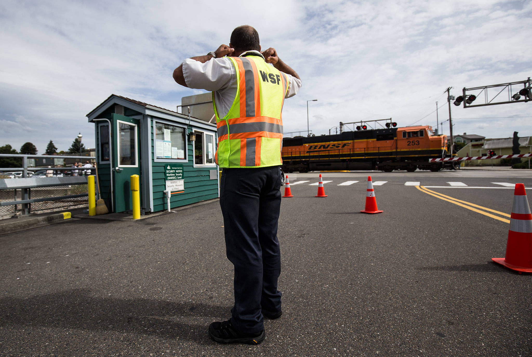 Washington State Ferries traffic attendant Brian Green plug his ears as a train blows its horn while heading south at the Edmonds Ferry dock on Friday, Sept. 21, 2018 in Edmonds, Wa. While Amtrak and the Sounder keep to a fixed schedule, the BNSF trains randomly block traffic when heading north or south. (Andy Bronson / The Herald)