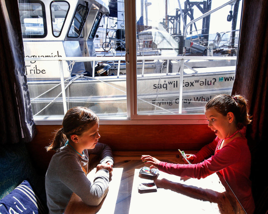 Bathed in sunlight streaming through the marina and the window of their Cruise-A-Home, Arianna, 10 (right) reacts to her hand while playing a card game with Joy, 11, at the family table, which converts each night to serve as their mom and dad’s bed. (Dan Bates / The Herald)

