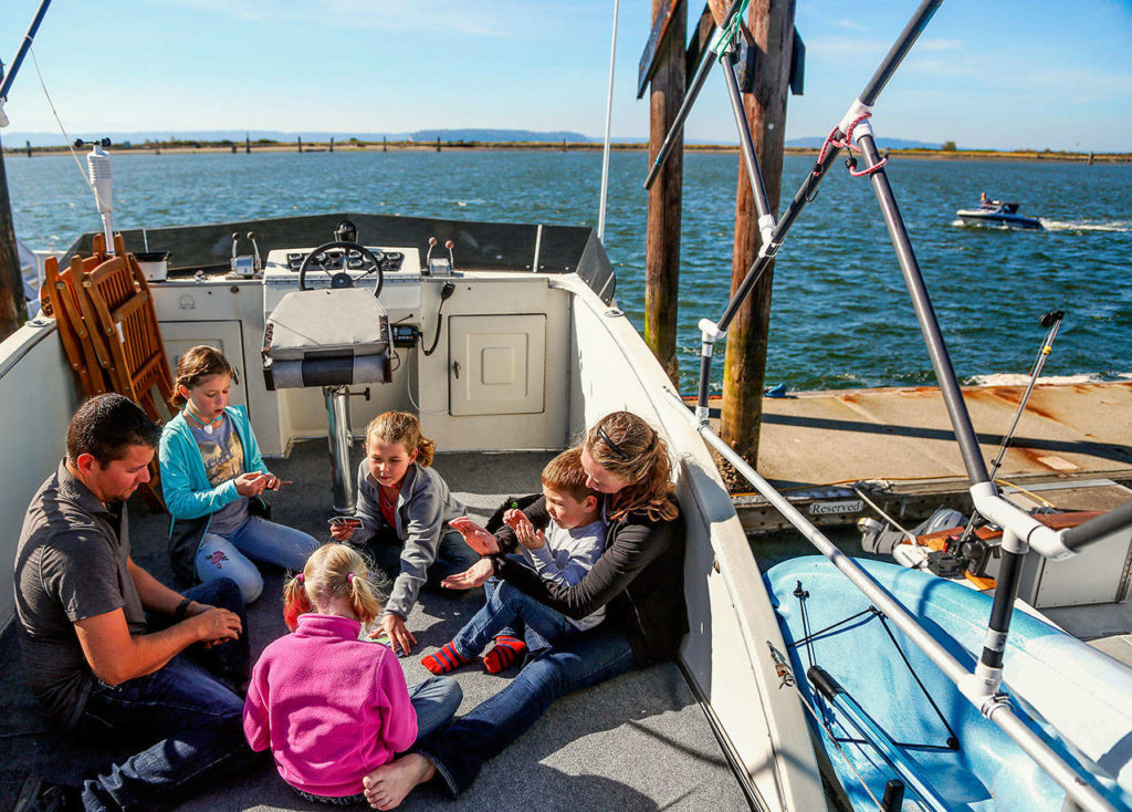 Ryan and Jacy Taisey and their four children play Uno on the upper deck floor of their 1976 Cruise-A-Home at the Everett Marina Tuesday. They bought the boat in 2017 after seven years in a rented house in Woodinville. The kids are homeschooled. From left clockwise, are Ryan, Joy, 11, Arianna, 10, Caleb, 4, Jacy, and Felicity, 7. (Dan Bates / The Herald) (Dan Bates / The Herald)
