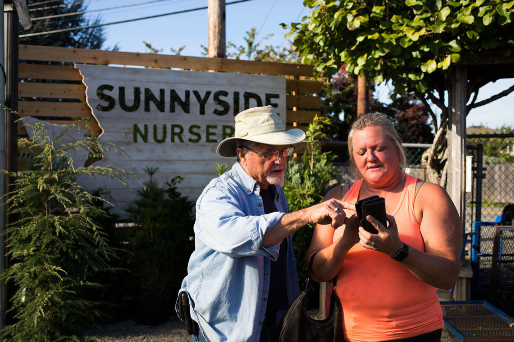 Owner Steve Smith looks at backyard photos with customer Carla Clemetson by a new vertical garden backdrop at Sunnyside Nursery on Tuesday in Marysville. The nursery has been in operation for 70 years. (Andy Bronson / The Herald)
