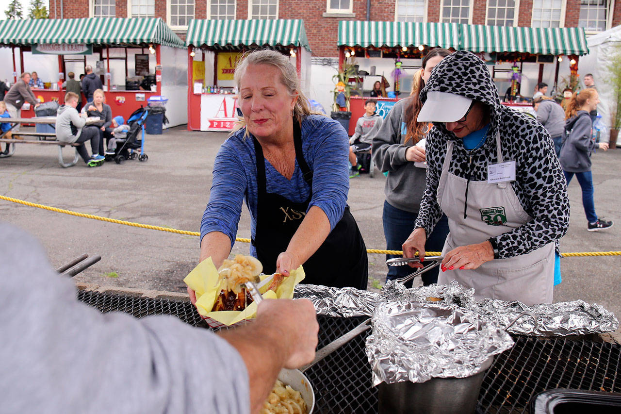 Michelle Eubank (left) gets sautéed onions with Sharon Burnham during the Everett Sausage Fest in 2017. The 42nd annual event kicks off Friday and runs through the weekend. It offers a secret recipe of sauerkraut, homemade German sausage, hand-dipped corn dogs and more. (Kevin Clark / Herald file)