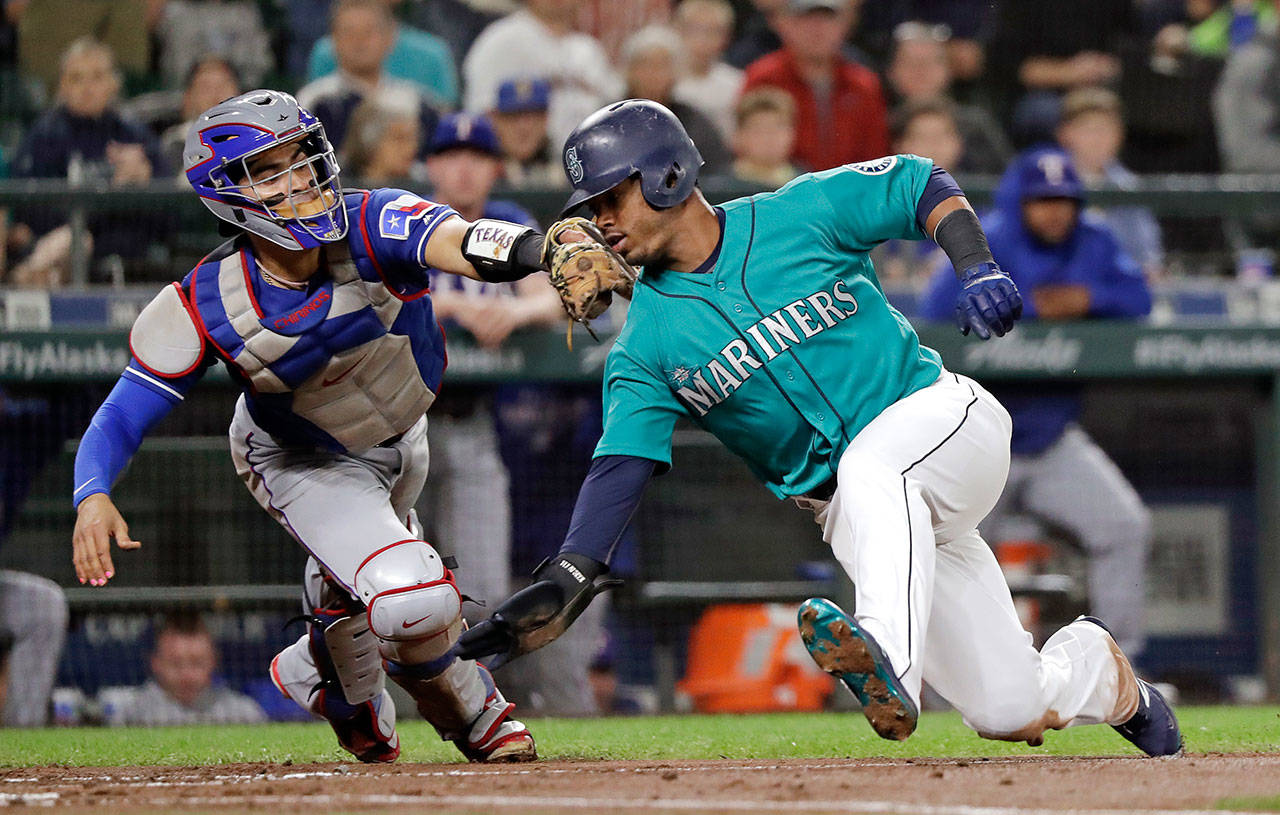The Mariners’ Jean Segura (right) avoids a tag by Rangers catcher Robinson Chirinos while sliding safely home in the second inning of a game Sept. 28, 2018, in Seattle. (AP Photo/Elaine Thompson)