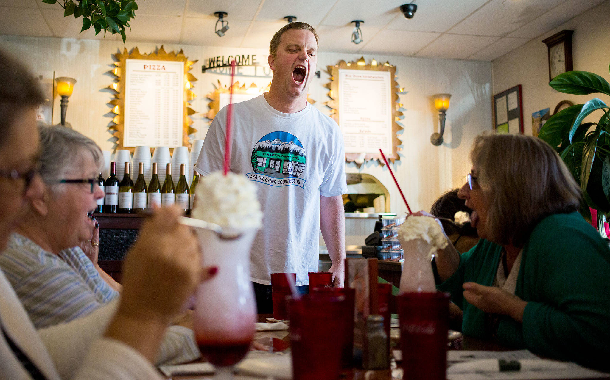 Program coordinator Eric Wollan dares Paula Darrow (right) to eat the whipped cream off her Italian soda like a shark during a group trip from the Everett Senior Center to Contos Pizza & Pasta on Sept. 17 in Lake Stevens. (Andy Bronson / The Herald)