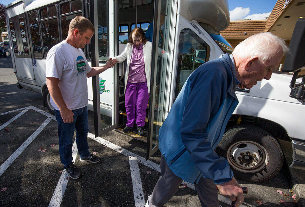 Program coordinator Eric Wollan helps Carolyn Crossman down from the shuttle bus as Bob Beil, 95, heads for the front door during a group trip from the Everett Senior Center to Contos Pizza & Pasta on Sept. 17 in Lake Stevens. (Andy Bronson / The Herald)
