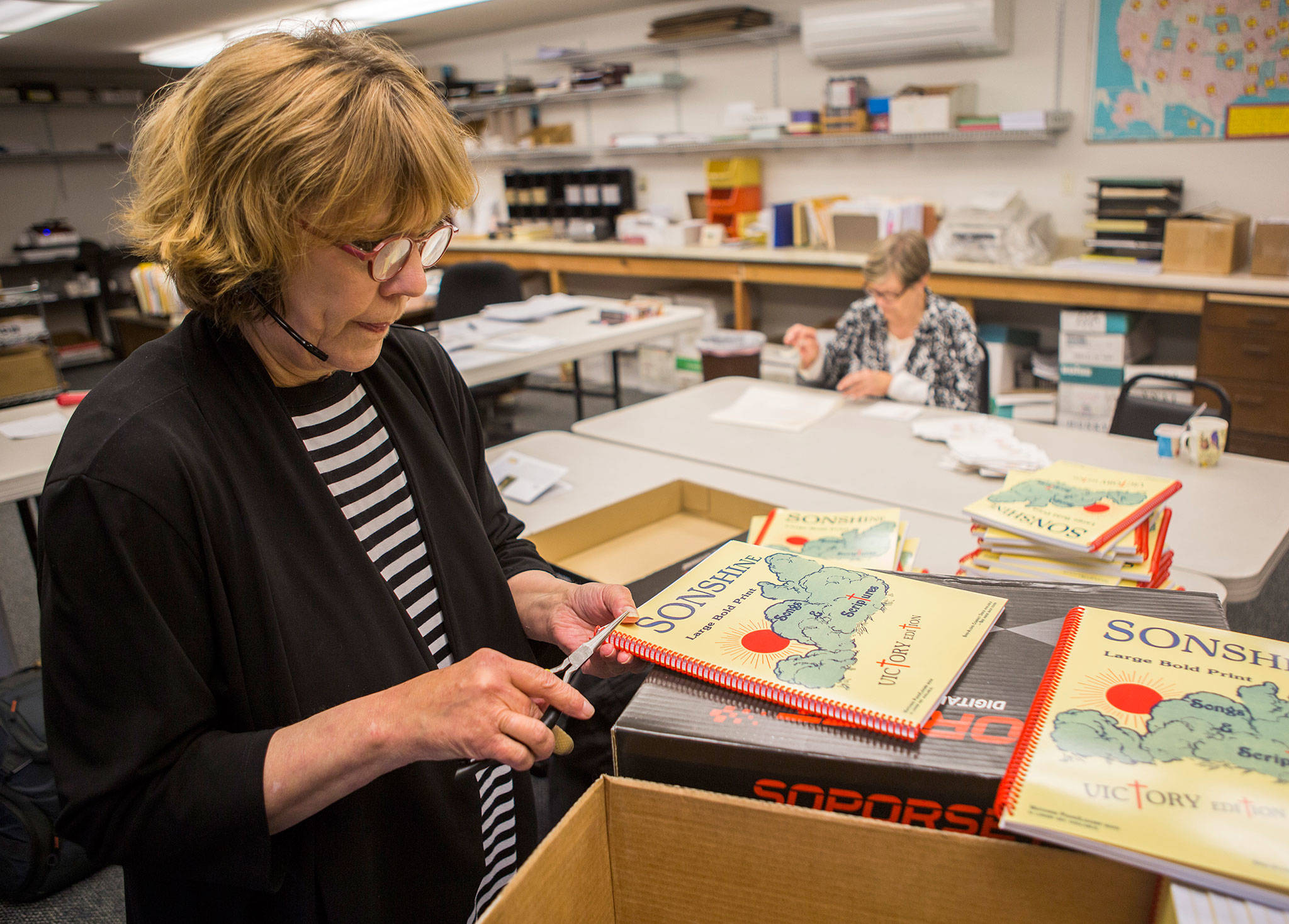 Patty Brinkerhoff works on the binding of recently finished song books at the Sonshine Society office on Sept. 26, 2018 in Everett, Wa. (Olivia Vanni / The Herald)