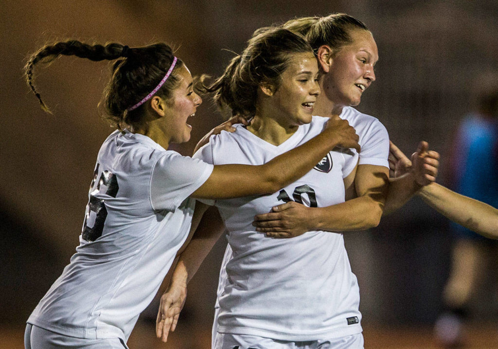 Cedarcrest’s Lauren Miller (left) and Piper Parish (right) hug teammate Sarah Hommas (center) after Hommas scored a goal against Snohomish during a game on Sept. 25, 2018, in Snohomish. (Olivia Vanni / The Herald)
