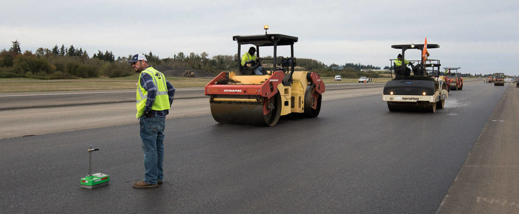 Jake Pittman keeps an eye out for steamrollers as he uses a nuclear density gauge to measure the compaction of the asphalt on the the runway at Paine Field on Oct. 3. (Andy Bronson / The Herald)
