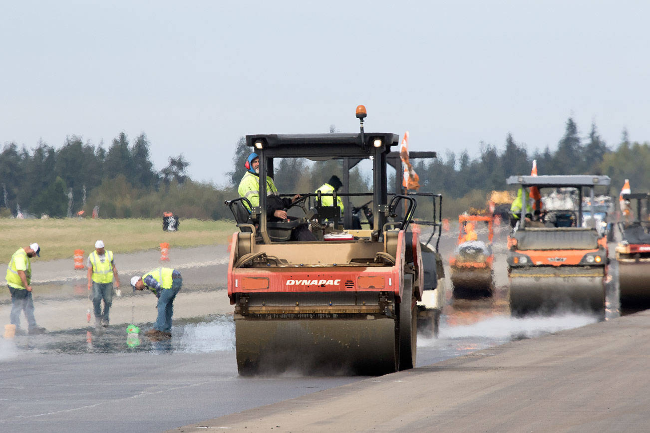 One of nearly a dozen steamroller operators reverses down down the runway at Paine Field while workers check compaction of the new asphalt on Wednesday, Oct. 3, 2018 in Everett, Wa. Workers spent the week milling and repaving a swath of the nearly two-mile runway that was 65 feet wide and 8,000 feet long. (Andy Bronson / The Herald)