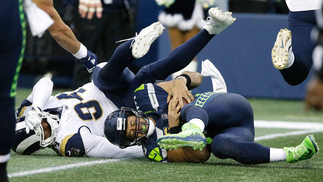 Seahawks quarterback Russell Wilson (right) is sacked by Rams outside linebacker Robert Quinn during a game on Dec. 17, 2017, in Seattle. (AP Photo/Elaine Thompson)