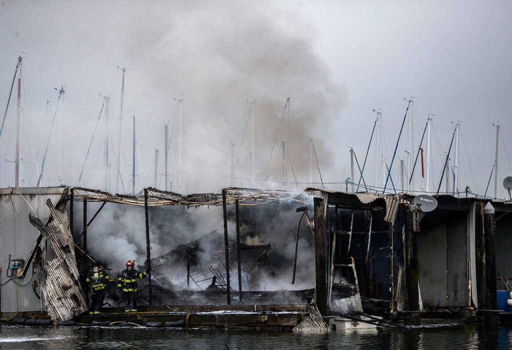 Firefighters stand on a dock next to a boat that burned in a fire Oct. 8, at the Port of Everett marina. (Olivia Vanni / The Herald)
