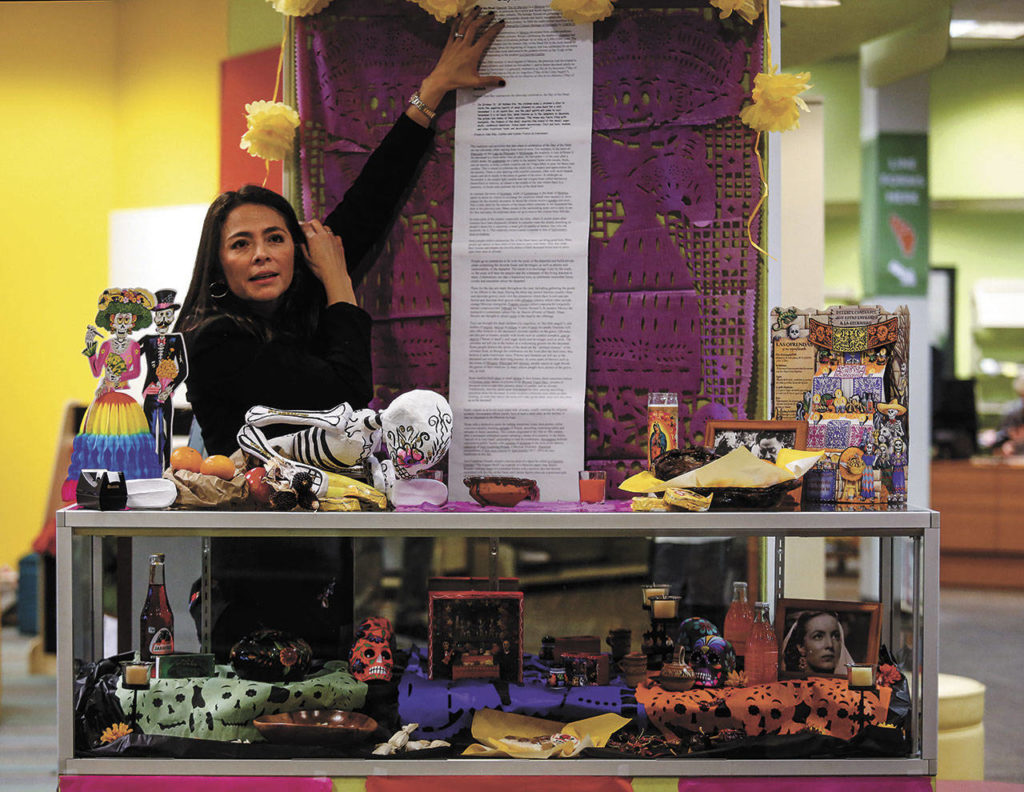 Julieta Altamirano-Crosby waits for her friend, Maria Casey, to bring her a staple gun to attach information about the Day of the Dead on a display at Lynnwood Library in 2017. (Dan Bates / The Herald)
