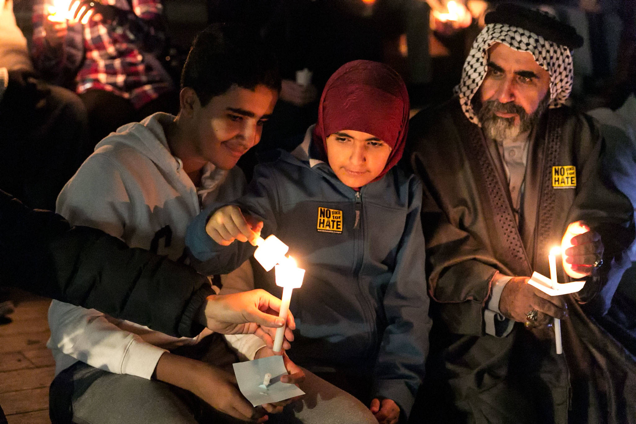 Muhammad Al-ali (left to right) Bentalha Al-Ali and Lafti Al-Ali work to light their candles during the interfaith candlelight vigil Thursday night at the Snohomish County Courthouse campus. (Kevin Clark / The Herald)