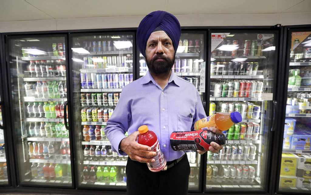 In this Oct. 1 photo, shop owner Prem Singh holds several soft drinks as he poses for a photo in front of a drink cooler in his convenience store in Kent. (AP Photo/Elaine Thompson, file)

