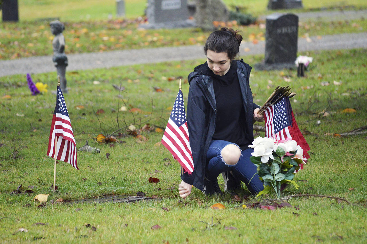Photos by Laura Guido / Whidbey News-Times                                 Alexis Kunze, a freshman NJROTC member, plants a flag near the grave of a veteran Nov. 3 at Maple Leaf Cemetery.