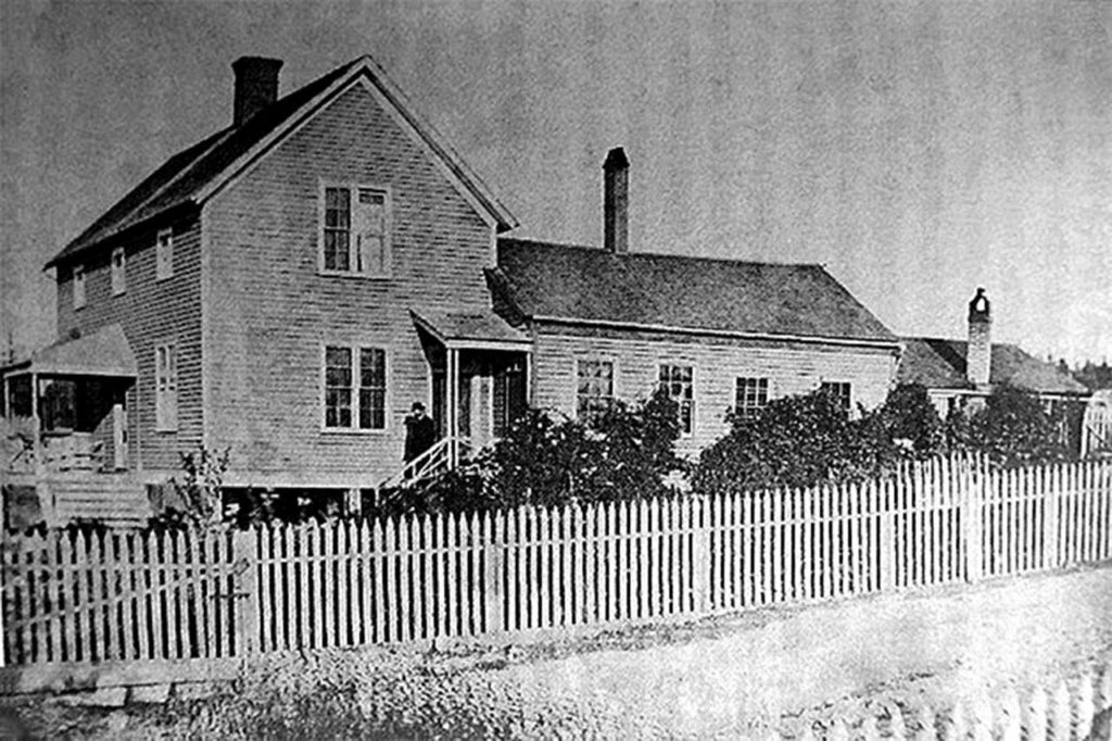 A man, most likely Col. Granville O. Haller, stands on the front steps of the Haller House in this circa 1870 photo. Note the original Brunn House attached at the rear. (Historic Whidbey)

