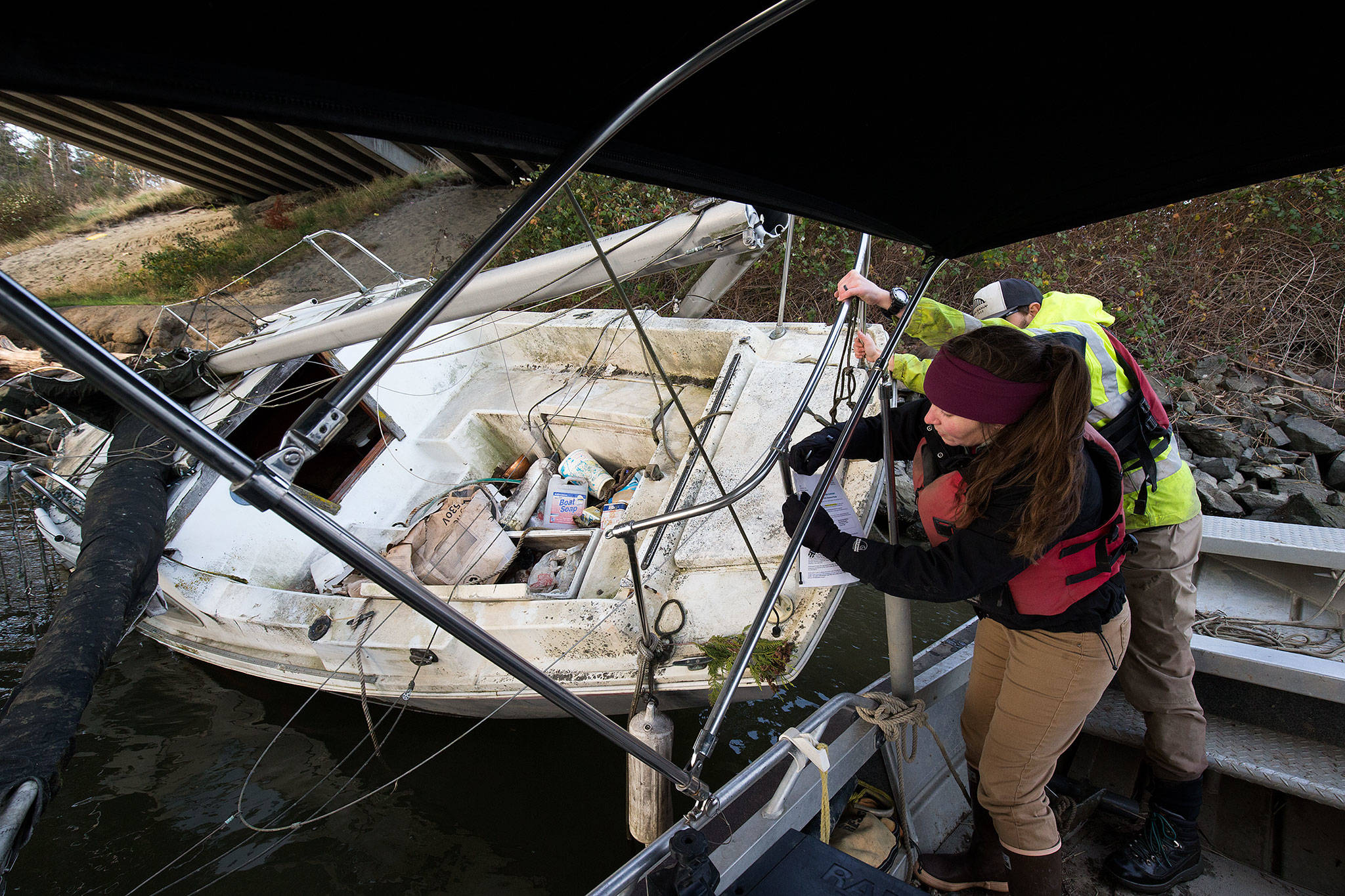 Kathleen Pozarycki, a senior planner with Snohomish County, and Luke Hanna, a biologist with the county’s surface water management division, post a 30-day notice on a sailboat washed up under an I-5 bridge on Tuesday. During storms a few weeks ago, the sailboat floated an estimated three miles downstream from where it was first spotted. (Andy Bronson / The Herald)