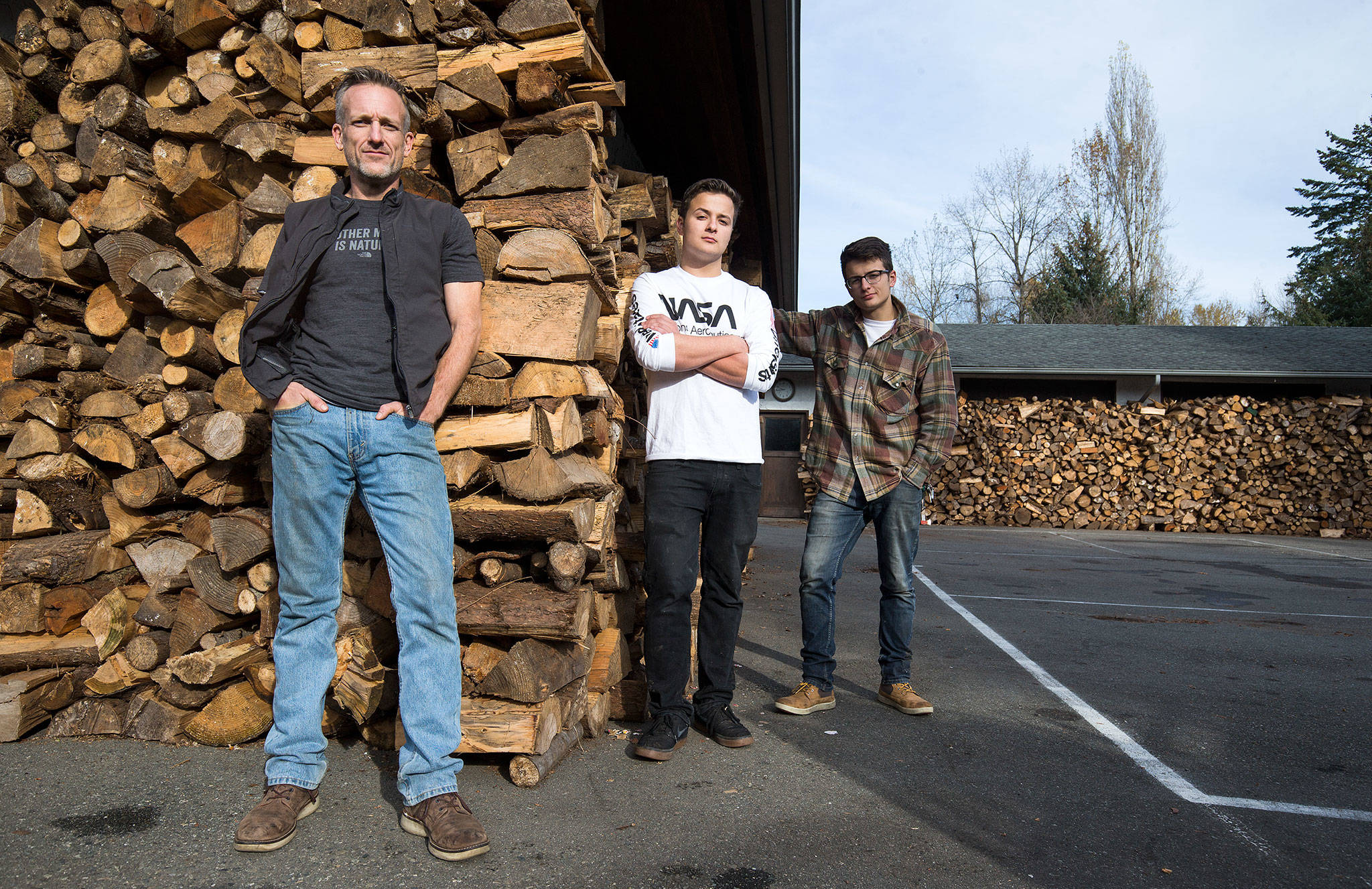 Shane McDaniel and his twin sons, Harrison and Henry, 20, stand by the wood stacked in front of their Lake Stevens home. They started with 40 cords of wood and are giving it out to those in need. The men spent months chopping the wood with the help of several friends. (Andy Bronson / The Herald)
