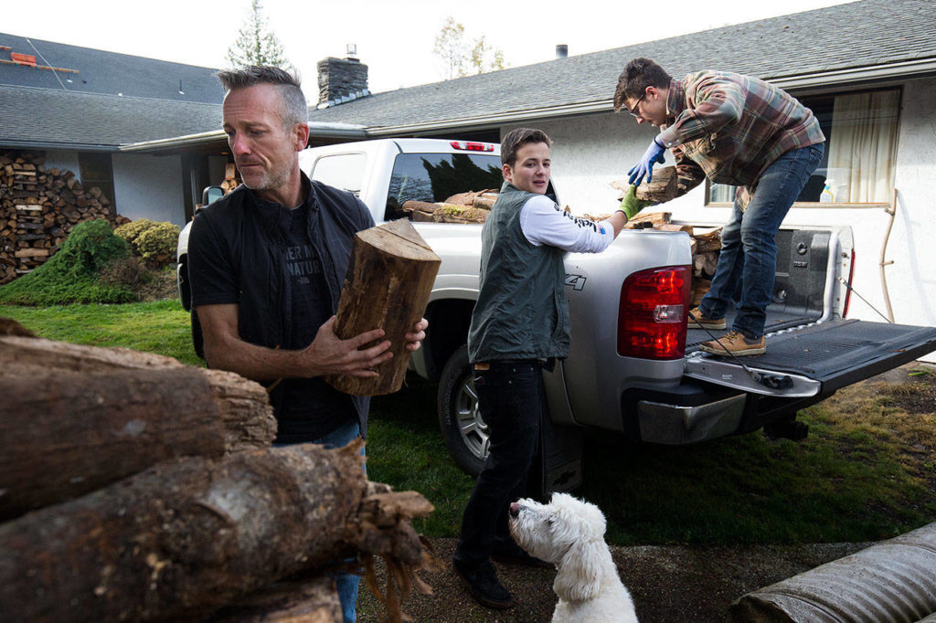 Shane McDaniel and his twin sons, Harrison, center, and Henry, 20, load up a truck full of wood at their Lake Stevens house on Monday. McDaniel started with 40 cords of wood and is giving it out to those in need. The men spent months chopping the wood with the help of several friends. (Andy Bronson / The Herald)
