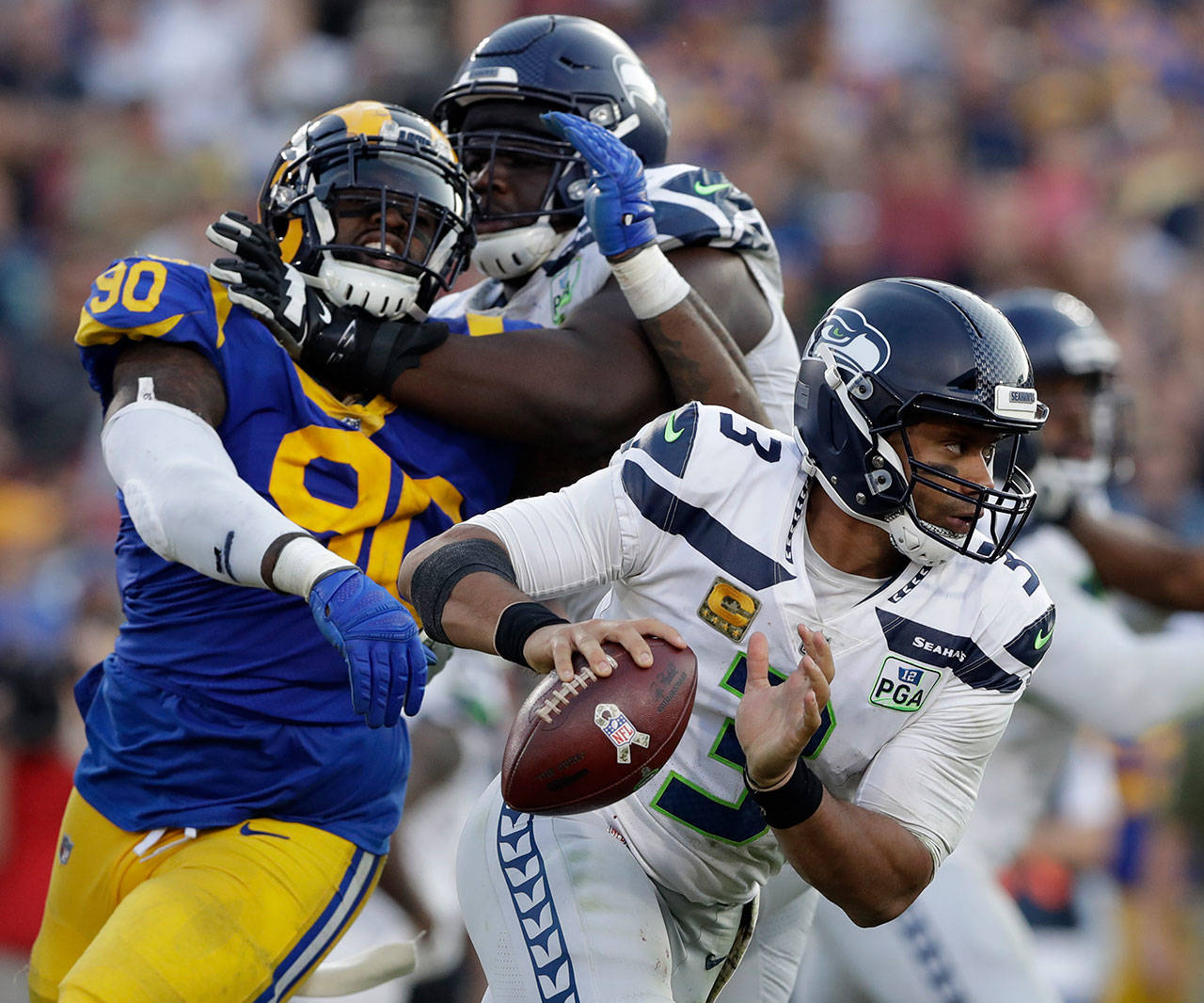 Seahawks quarterback Russell Wilson (3) scrambles away from pressure as Rams defensive end Michael Brockers (90) battles Seahawks offensive tackle Germain Ifedi (right) during game on Nov. 11, 2018, in Los Angeles. (AP Photo/Alex Gallardo)