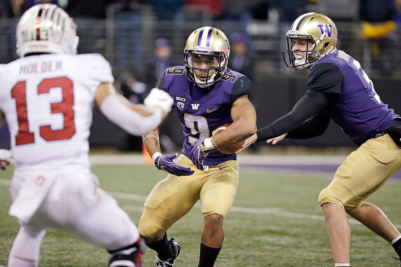 Washington quarterback Jake Browning (right) hands off to Myles Gaskin as Stanford defender Alijah Holder watches during a game Saturday in Seattle. (Elaine Thompson / Associated Press)