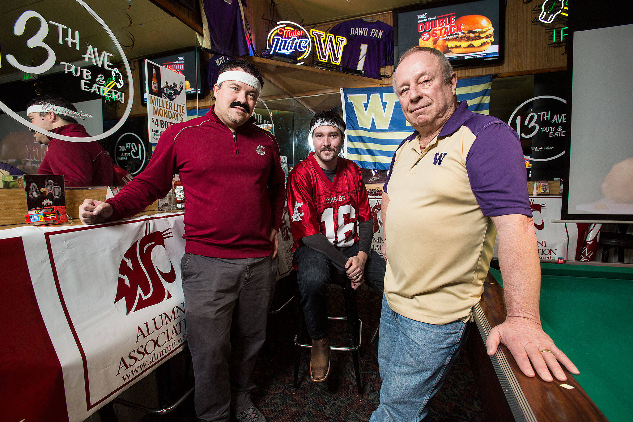 Kris Baier, WSU Alumni Association Snohomish President, left, Randy Bolerjack and Wayne Larson, owner of 13th Ave Pub & Eatery are ready for the Apple Cup on Wednesday, Nov. 21, 2018 in Lynnwood, Wa. Cougar fans have been gathering to watch football games in Lynnwood, owned by diehard Huskies fan Larson, resulting in a friendly rivalry. (Andy Bronson / The Herald)