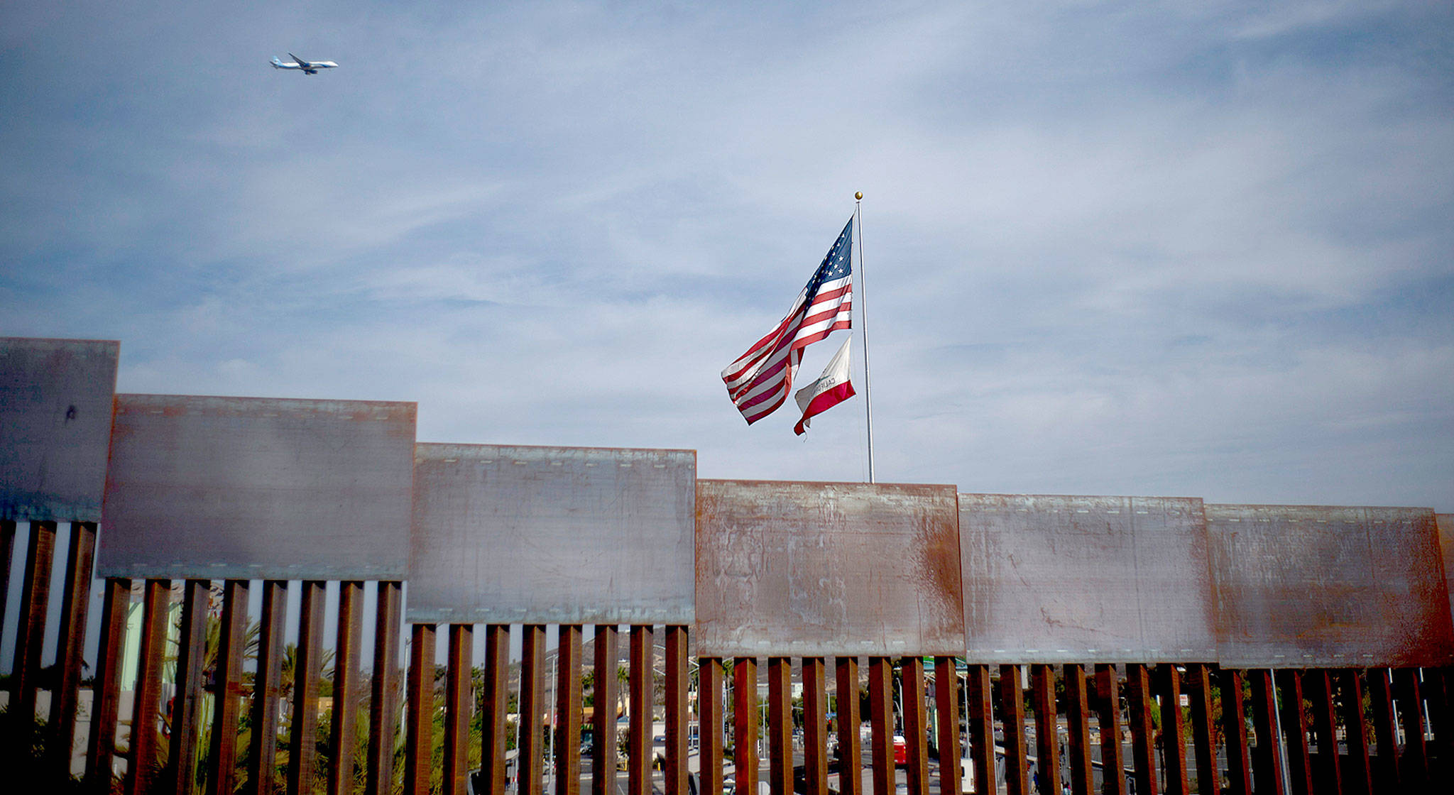 U.S. and California state flags fly behind the border wall, seen from Tijuana, Mexico, on Monday. (AP Photo/Ramon Espinosa)