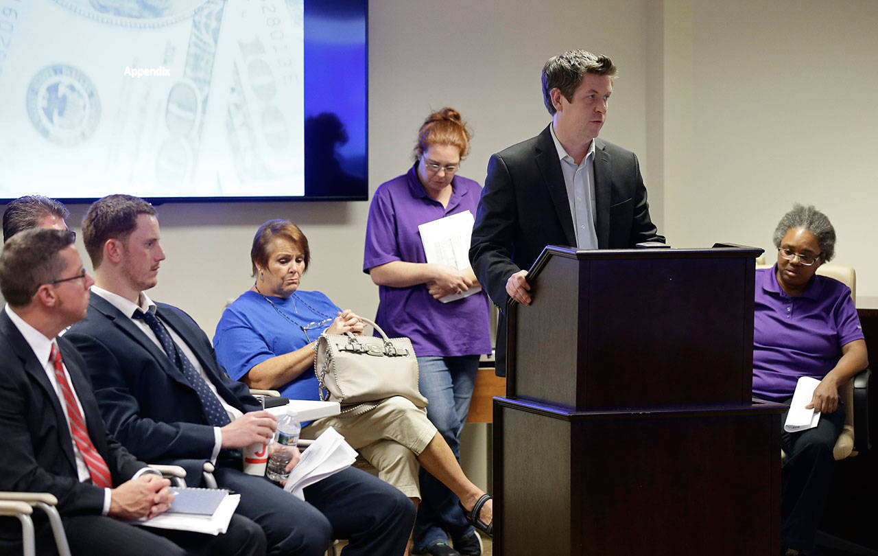 Jim Baker, a campaigner at the Private Equity Stakeholder Project speaks surrounded by three former Toys R Us employees during the public comments portion of an investment advisory committee meeting of the North Carolina Department of State Treasurer in Raleigh, N.C., Aug. 23. Two private equity owners of Toys R Us announced Tuesday, Nov. 20, that they will be handing over a $20 million hardship fund to the thousands of former workers left jobless and without severance after the chain liquidated in June. (AP Photo/Gerry Broome)