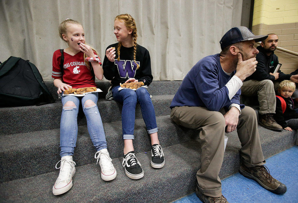Sporting opposing team gear, Lauren Rice and Avery Kirkman (right) enjoy chatting together as Dutch Hill Elementary held an Apple Cup-themed Dads ‘n Donuts event, with the gym decked out in Cougar and Husky colors, on Nov. 21, 2018, in Snohomish. (Andy Bronson / The Herald)
