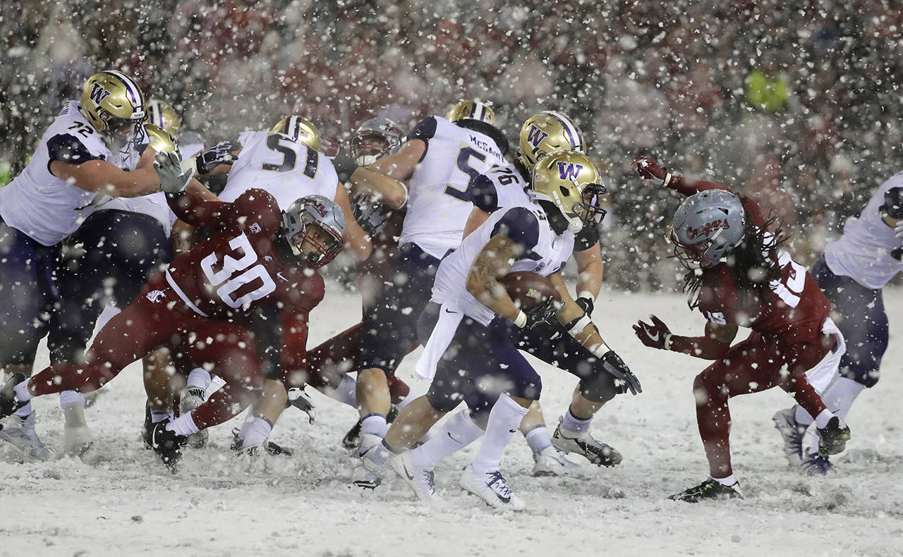 Washington running back Myles Gaskin (center) rushes past Washington State defensive lineman Nnamdi Oguayo (30) and linebacker Jahad Woods (right) during the second half of the Apple Cup on Friday in Pullman. Washington won 28-15. (AP Photo/Ted S. Warren)