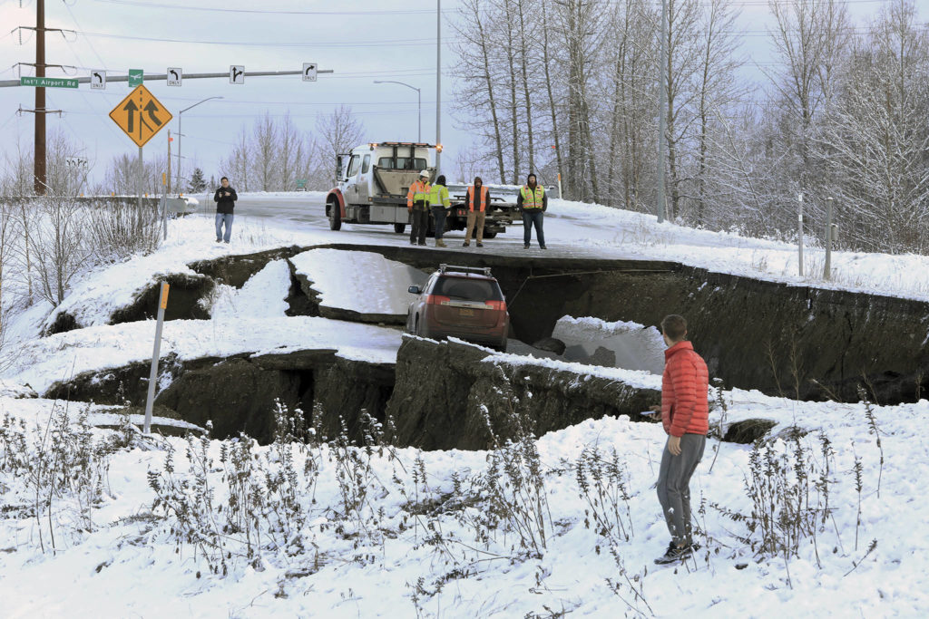 Highway workers and spectators look at a car stuck on a section of an off-ramp that collapsed during an earthquake Friday morning in Anchorage, Alaska. The driver was not injured attempting to exit Minnesota Drive at International Airport Road. (AP Photo/Dan Joling)

