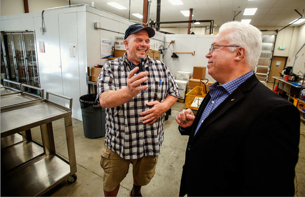 After making deliveries and returning to the food storage areas at Homage Senior Services, Meals on Wheels driver Bruce Rhodes (left) shares something he captured on his cellphone camera with CEO Steve McGraw. (Dan Bates / The Herald) 
