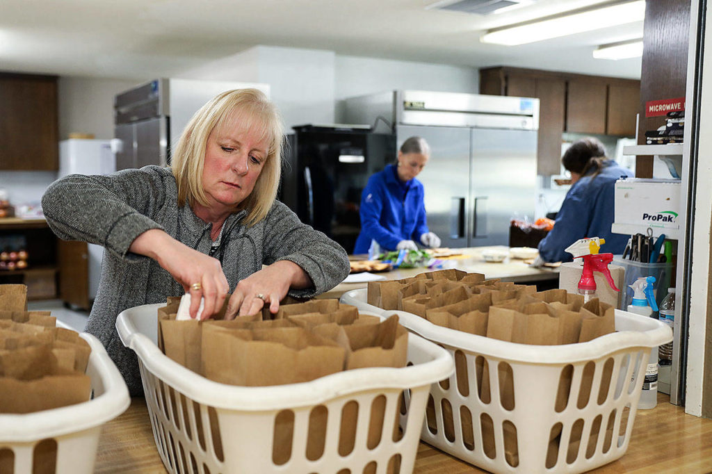 Sandie Cooper, a volunteer with Hands Together and the Brown Bag Brigade, preps the lunch sacks inserting a juice box and granola bar into each. (Lizz Giordano / The Herald)
