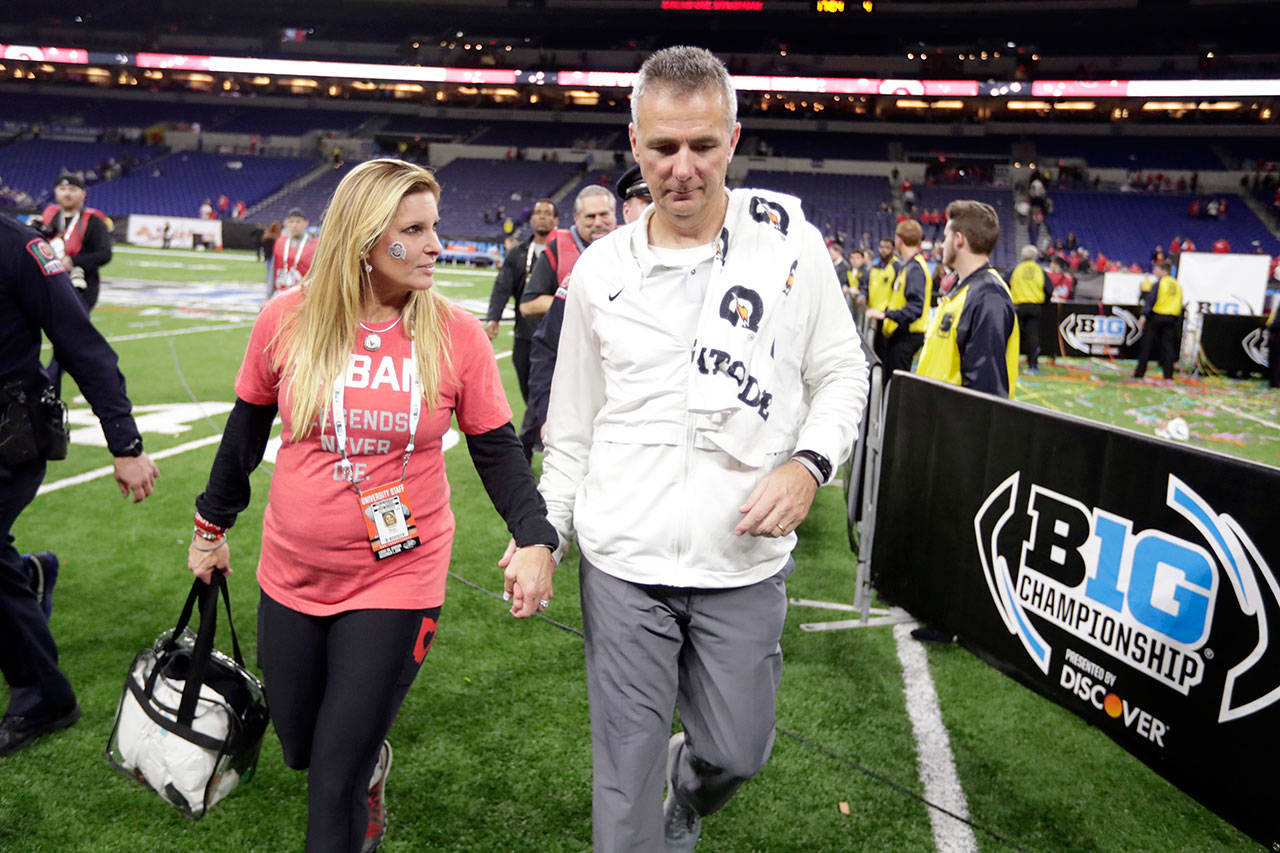 Ohio State football coach Urban Meyer walks off the field with his wife, Shelley Meyer, early Sunday after the Buckeyes defeated Northwestern in the Big Ten championship. (AP Photo/Michael Conroy)