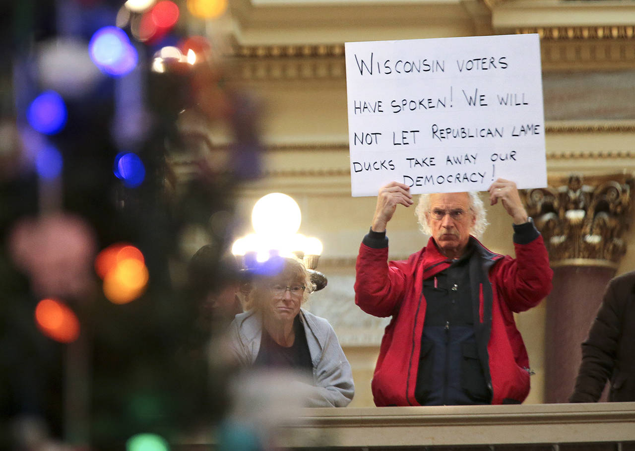Bob Kinosian, from Wauwatosa, Wisconsin, holds up a sign during the state Christmas Tree lighting ceremony in state Capitol Rotunda Tuesday on Dec. 4 in Madison. The Senate and Assembly are set to send dozens of changes in state law to Gov. Scott Walker’s desk. (Steve Apps / AP)