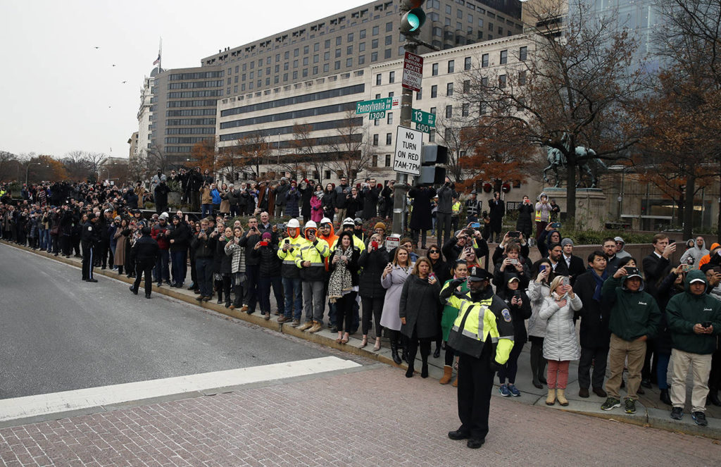 People watch as the hearse carrying the flag-draped casket of former President George H.W. Bush passes Freedom Plaza on its way to a State Funeral at the National Cathedral on Wednesday in Washington. (AP Photo/Alex Brandon, Pool)
