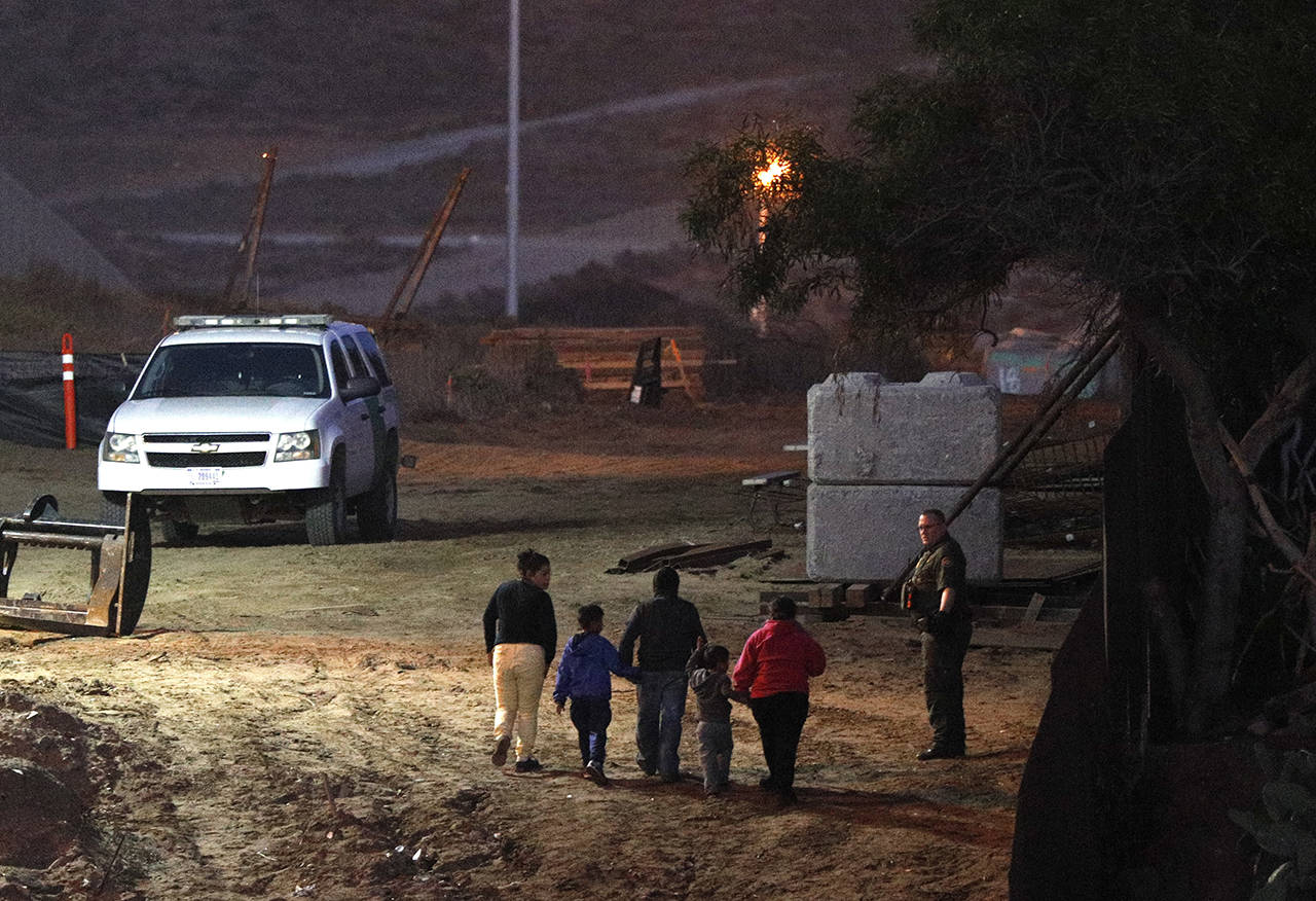 Migrants traveling with children walk up a hill to a waiting U.S. Border Patrol agent just inside San Ysidro, California, after climbing over the border wall from Playas de Tijuana, Mexico, on Dec. 3. (AP Photo/Rebecca Blackwell)