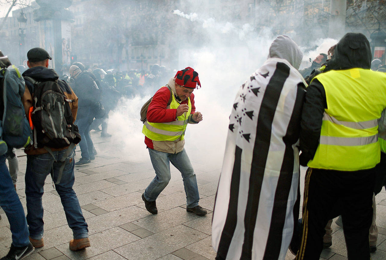 A tear gas canister falls among demonstrators wearing yellow vests Saturday in Paris. Prized Paris monuments and normally bustling shopping meccas locked down Saturday and tens of thousands of police took position around France, fearing worsening violence in a new round of anti-government protests. (AP Photo/Thibault Camus)