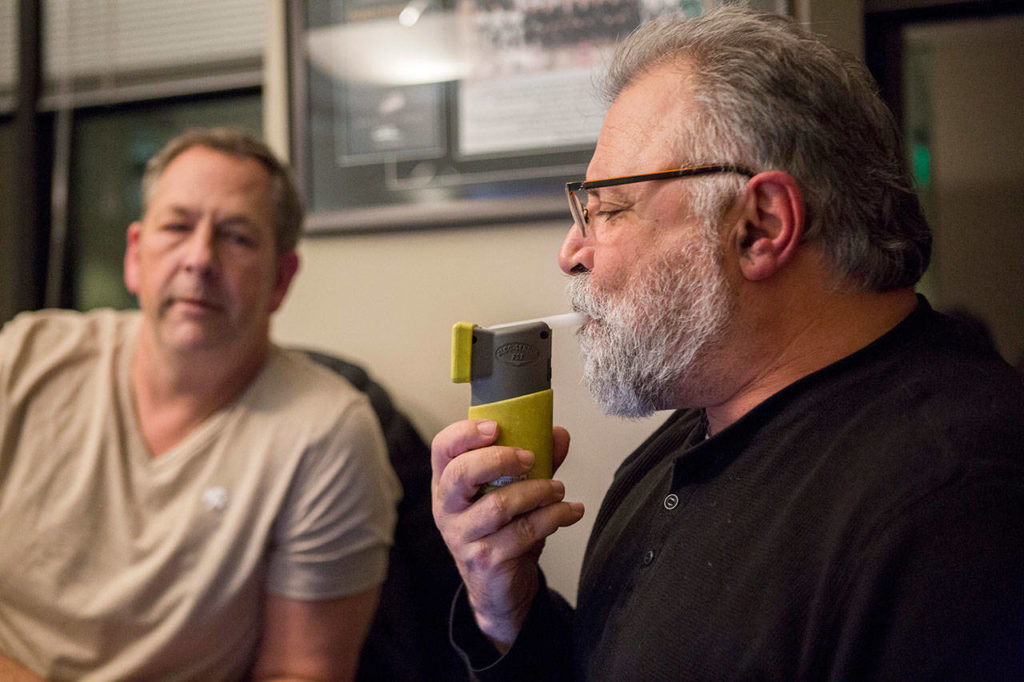 Lynnwood police officer Mark Brinkman watches as Maury Eskenazi blows into a breath test at the KRKO radio office in Everett. (Olivia Vanni / The Herald)
