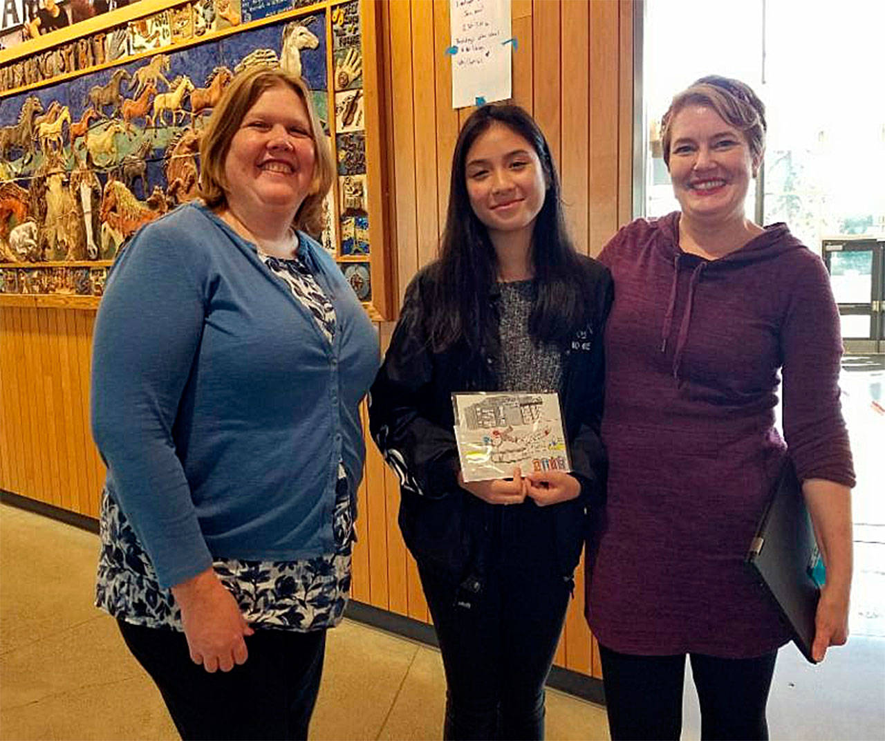 Trang Nguyen (center) is congratulated by Lynnwood Convention Center General Manager Sara Blayne and art teacher Amy Barnes on winning the center’s 2018 holiday greeting card competition. (Contributed photo)