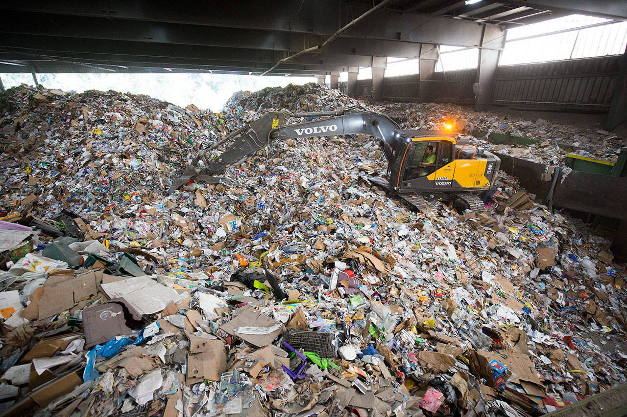 An excavator picks up recycled materials and then puts a load on a conveyor belt to be sorted and recycled at Waste Management’s Woodinville recycling center in August. China has tightened rules for what its recycling mills were accept, meaning more work for U.S. recyclers. (Andy Bronson / Herald file photo)