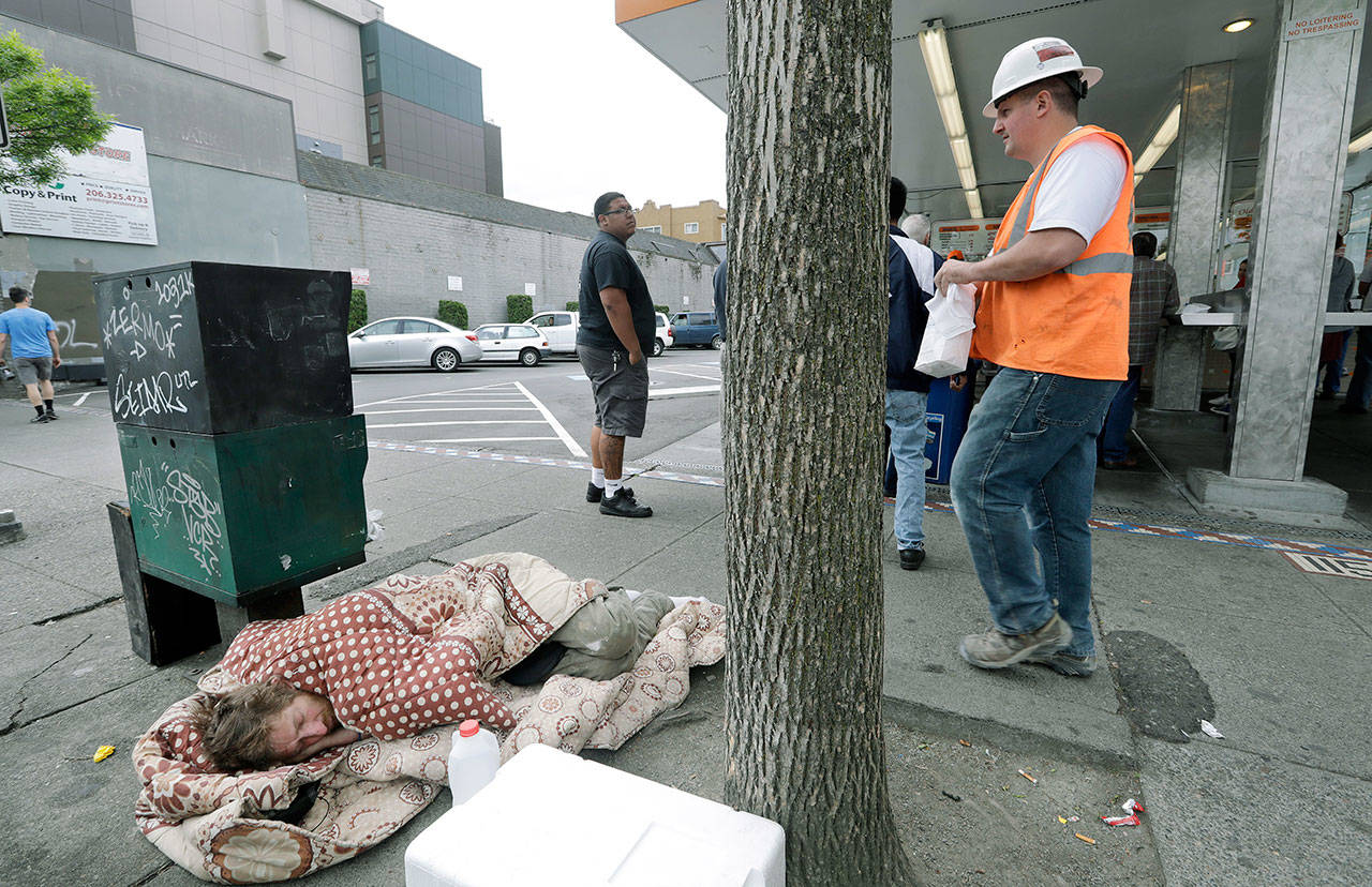 A man sleeps on the sidewalk as people behind line up to buy lunch at a Dick’s Drive-In restaurant in Seattle on May 24. A new federal report says the number of people living on the streets in Los Angeles and San Diego, fell this year, suggesting possible success in those cities’ efforts to combat the problem. Meanwhile, homelessness overall was up slightly across the country, including Seattle, although the report did not provide a complete picture of the problem. (AP Photo/Elaine Thompson, File)