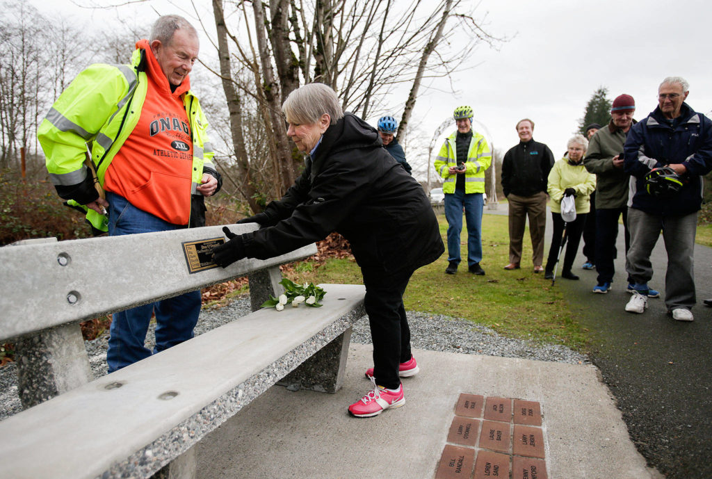 After laying down flowers Wednesday, Dec. 19, Ann O’Donnell touches a plaque with her late husband Dan’s name on it as family members and riders from “The Big Shots Bicycle Group” pay their respects at a bench in founder Dan O’Donnell’s name along the Centennial Trail in Arlington. (Andy Bronson / The Herald)
