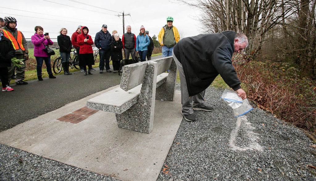 Friends, family and members of the “The Big Shots Bicycle Group” watch Jeff O’Donnell spread his father’s ashes behind a bench in Dan O’Donnell’s name along the Centennial Trail on Wednesday, Dec. 19, in Arlington. (Andy Bronson / The Herald)

