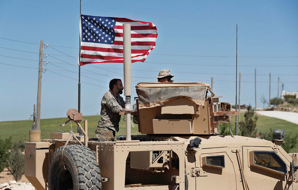 In this April 4 photo, a U.S-backed Syrian Manbij Military Council soldier (left) speaks with a U.S. soldier at a U.S. position near the tense front line with Turkish-backed fighters, in Manbij town, north Syria. (AP Photo/Hussein Malla)
